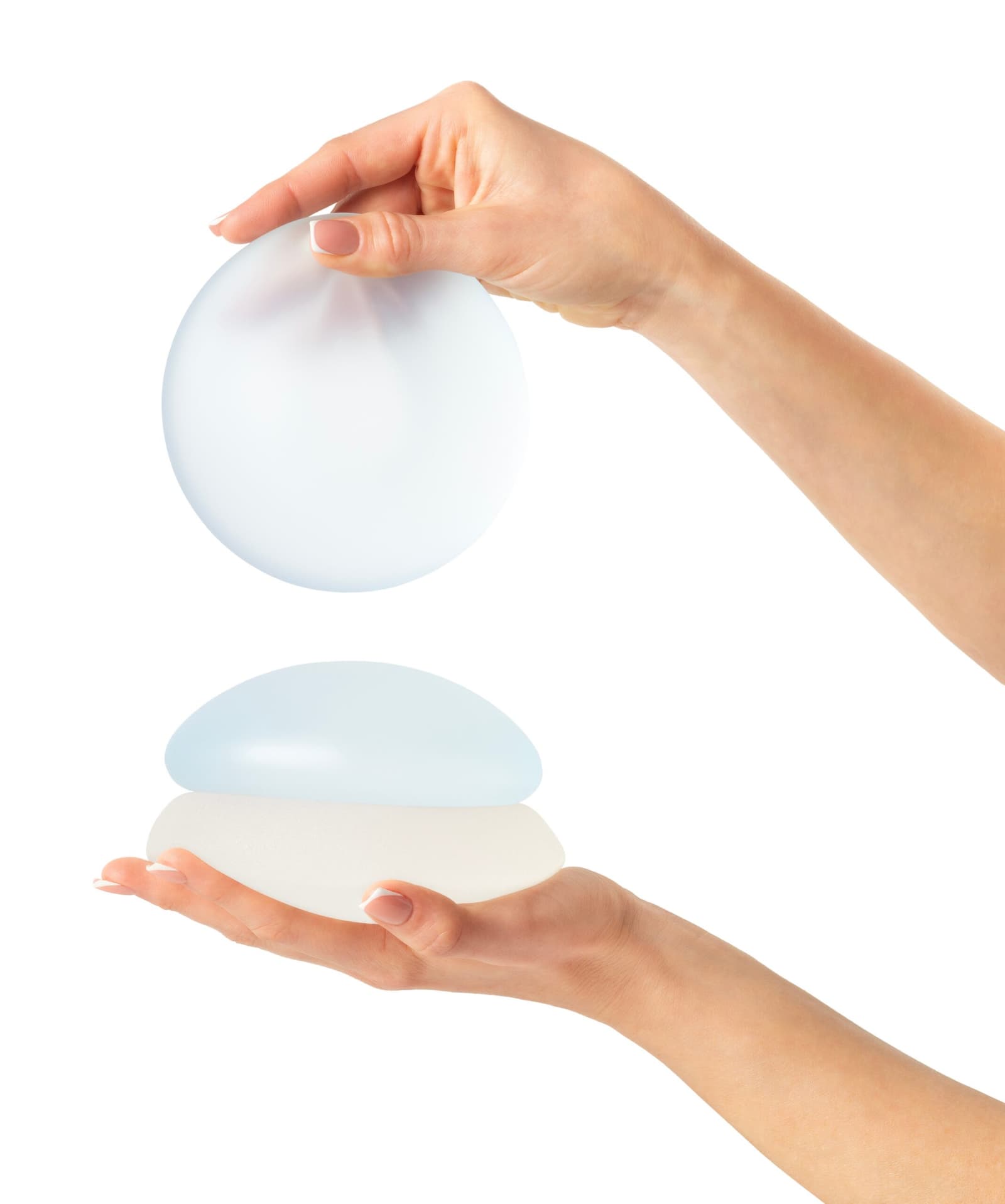 Hands holding round breast implants against a white background